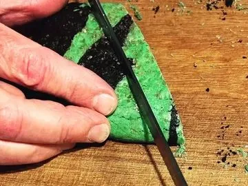 A person cutting a piece of cake with green frosting.