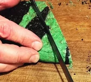 A person cutting a piece of cake with green frosting.